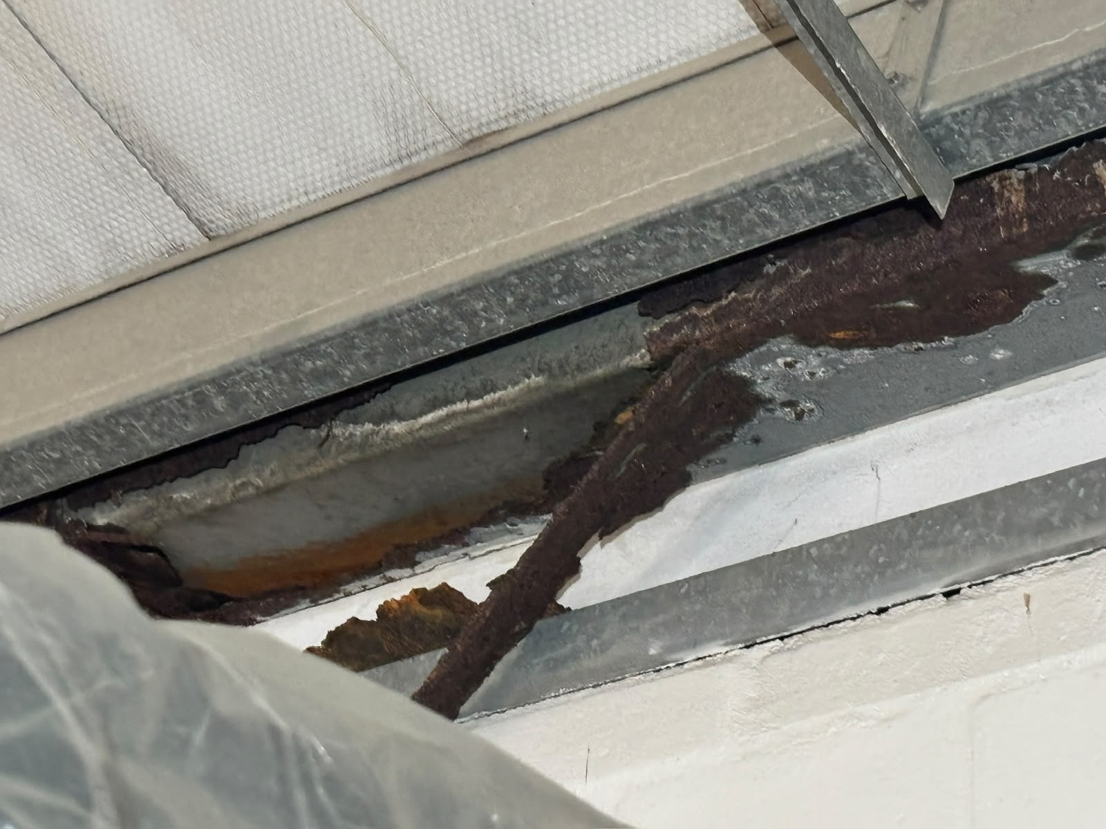 Rust spreading along the inside of a commercial box gutter above a ceiling